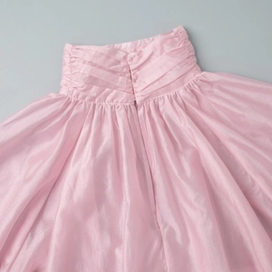 Close-up of pink pleated fabric detail showing lantern sleeve texture and soft pearly sheen