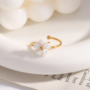 Detail eines verstellbaren Goldrings mit weißer Muschelblume auf weißem Tablett