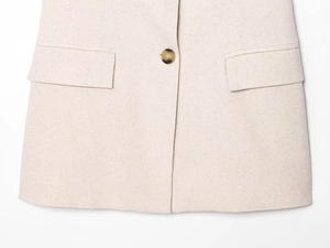 Dettaglio del gilet in lino con bottone ambra e tasche a pattina simmetriche in beige
