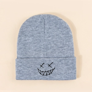 Detail of grey knitted beanie with black embroidered smiley face on folded brim
