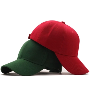 Close-up of red and dark green baseball caps featuring cotton twill texture and stitching