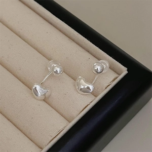 Macro shot of polished silver bean stud earrings on a soft beige jewelry cushion