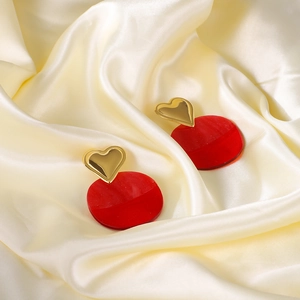 Trendy golden heart and red resin earrings displayed on a soft silk fabric background