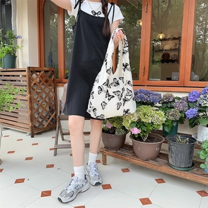 Detailed close-up of a white canvas tote bag with black butterfly prints in a garden setting