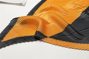 Macro detail of pleated silk scarf showing yellow and grey geometric color-block texture