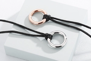 Minimalist polished silver and rose gold rings on black cord on a white cube pedestal
