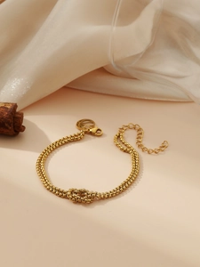 Close-up of golden double-layer chain bracelet with central knot design on silk background