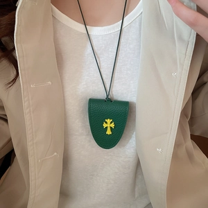 Detail of dark green leather glasses holder necklace with yellow cross charm on a model