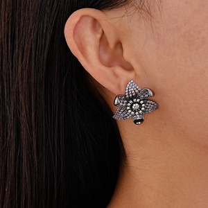 Detailed close-up of a vintage floral earring with purple and white cubic zirconia on a model