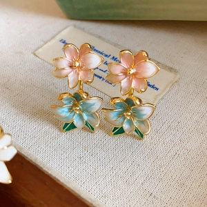 Macro detail of enamel flower earrings with gradient petals and green leaf accents