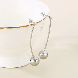Détail de longues boucles d'oreilles argentées avec sphères de 12mm sur un bol en céramique