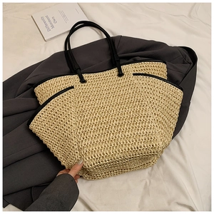 Detail of a beige straw tote bag with black handles on a white fabric and blazer