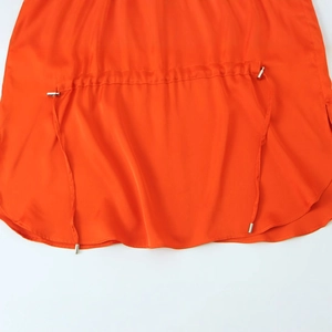 Close-up of orange silk satin shirt featuring metal drawstring tips and smooth fabric texture