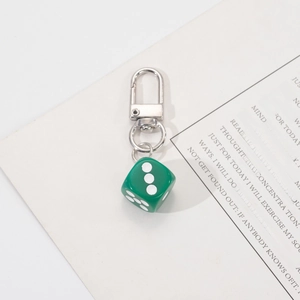 Detailed close-up of dark green dice keychain with silver metal lobster clasp on paper