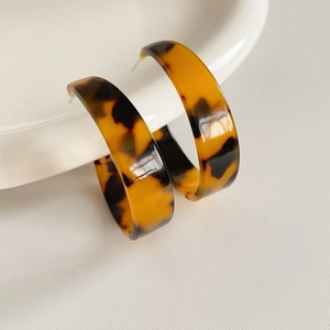 Close-up of tortoiseshell C-shaped resin earrings resting on a white ceramic plate
