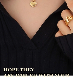 Detail of 18K gold-plated heart necklace and letter B ring on a black knit top