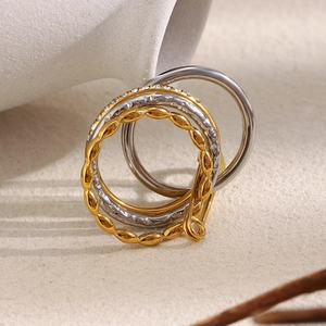 Detail of stacked ring set featuring twisted textures and zircon inlays on sand