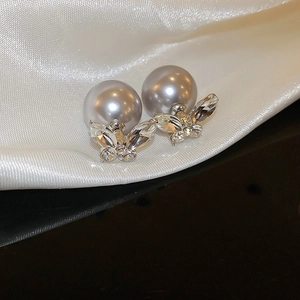 Macro detail of silver needle earrings featuring grey pearls and crystal bow accents