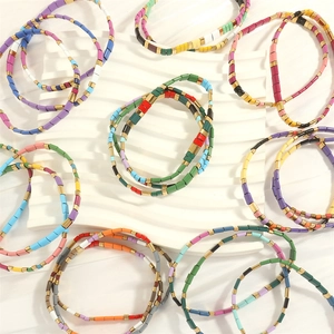 Close-up of colorful enamel tila bead bracelets displayed on a white textured tray
