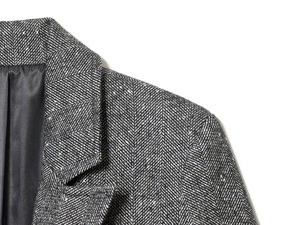 Detail of herringbone tweed texture on the collar and shoulder of this gray blazer jacket