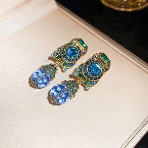 Macro shot of vintage gold ear clips featuring blue crystals and green cubic zirconia detail