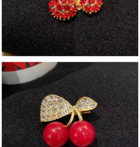 Detailed view of cherry brooch with red rhinestones and gold leaf setting on black fabric