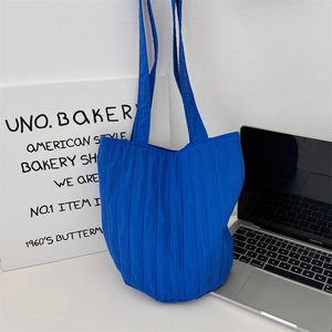 Detail van blauwe gewatteerde draagtas met verticale plooien naast laptop