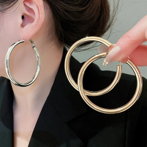 Detailed comparison of large gold and silver polished hoop earrings held in hand