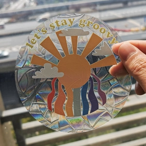 Macro shot of a holographic rainbow suncatcher sticker with 'let's stay groovy' text