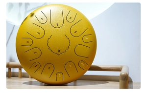 Close-up of a yellow steel tongue drum with numbered scales on a rustic wooden surface