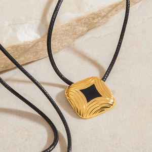 Detail of a square gold rippled pendant with black resin on a textured stone surface