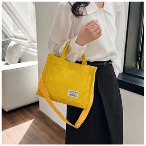 Detail of yellow corduroy handbag showing adjustable strap and white brand logo label