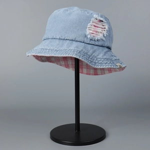 Detail of distressed denim bucket hat with pink plaid lining on black metal stand