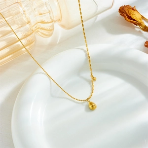Elegant gold teardrop necklace with green gemstone on ball chain in white ceramic dish