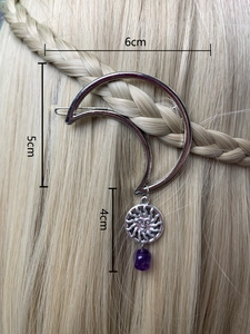 Detail view of a silver moon hair clip with sun charm and purple bead on braided hair