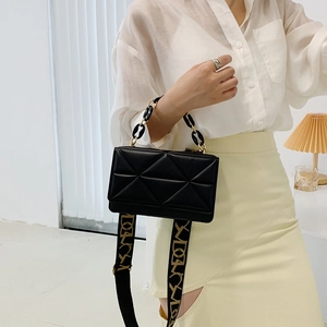 Detail of black quilted crossbody bag with golden chain handle and jacquard strap
