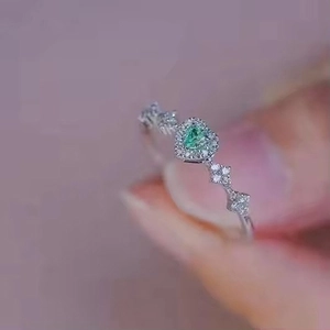 Close-up of heart-shaped green gemstone ring with pavé diamonds on a silver band