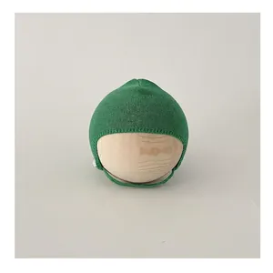 Detailed knit texture of a green baby bonnet with ties on a minimalist display stand