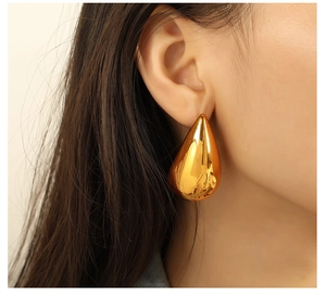 Close-up of a large gold teardrop earring made of titanium steel worn by a model