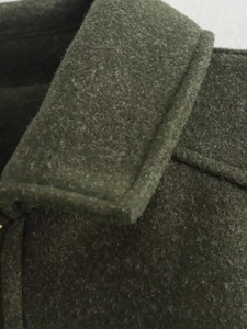 Close-up of olive green wool blend jacket fabric showing thick texture and collar stitching
