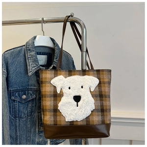 Detail of wool plaid tote bag featuring a cute plush dog patch and brown leather base