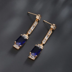 Detail shot of luxury gold earrings featuring large blue rectangular gemstones and cubic zirconia