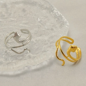 Macro shot of gold and silver hollow snake-shaped adjustable rings on a glass tray