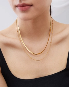 Close-up of a double-layered gold titanium necklace featuring a flat snake chain and bead link