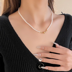 Detail of vintage small white pearl necklace with gold beads on black V-neck sweater