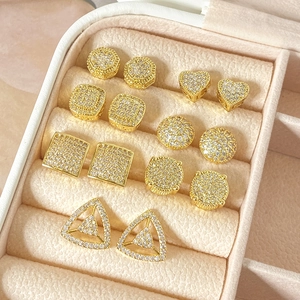Golden geometric stud earrings set with white zircon stones in a jewelry box display