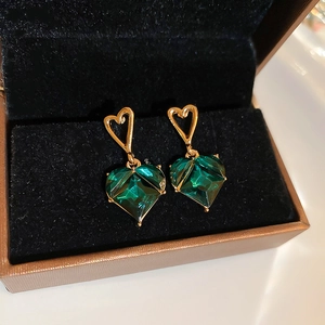 Detail of emerald green heart-shaped earrings with gold plating on a black velvet box