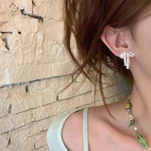 Gros plan de boucles d'oreilles nœud en argent avec texture dentelle portées à l'oreille