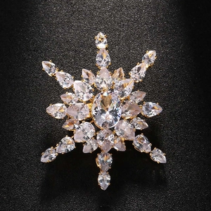 Close-up of golden snowflake brooch with sparkling crystals on black textured surface