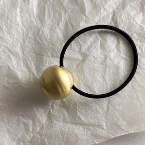 Détail d'une sphère dorée mate sur élastique noir pour queue de cheval sur papier